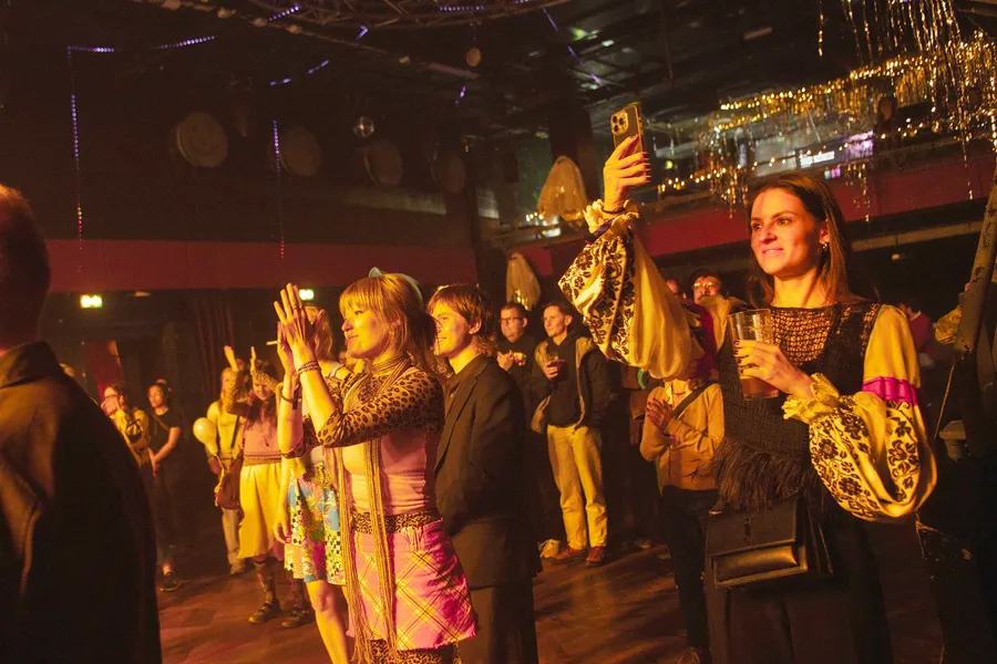 A crowd in patterned costume filming a performance on their phones
