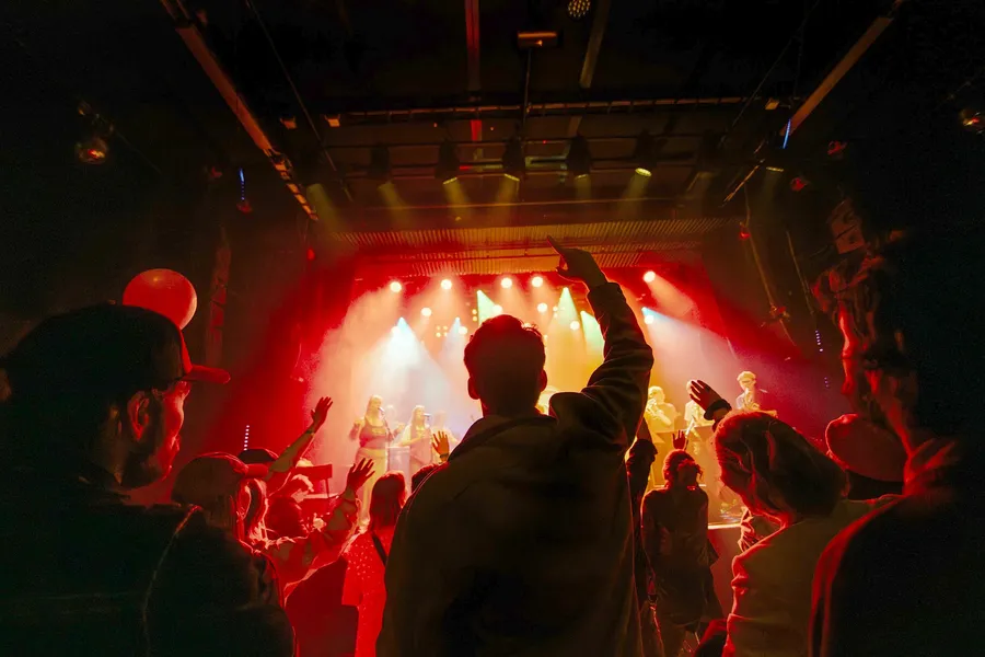 Silhouetted heads and raised arms against a red stage