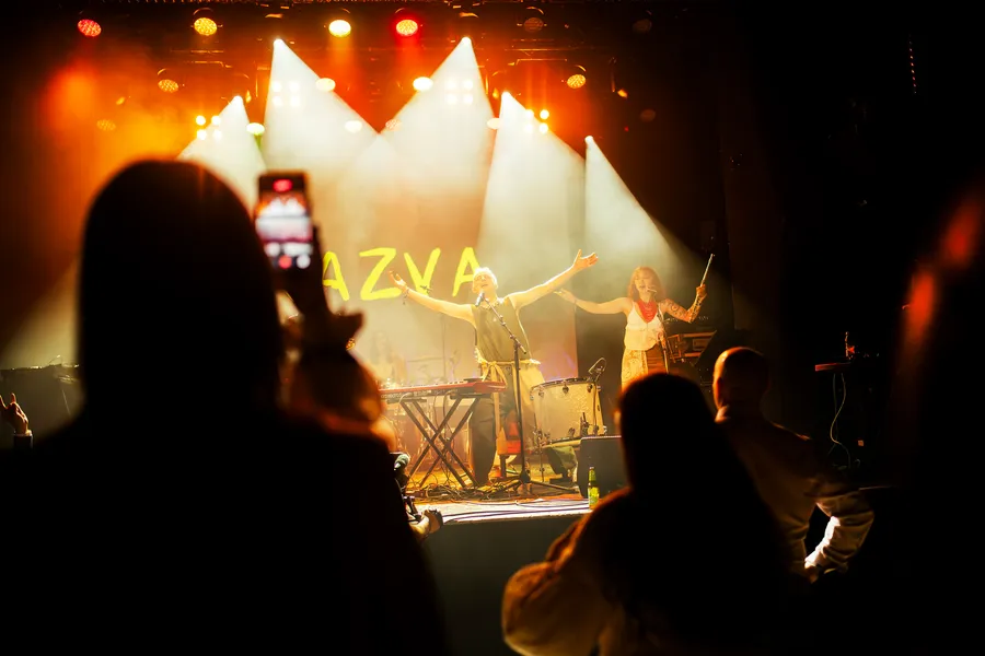 A singer on a gold-lit stage seen past a silhouetted audience