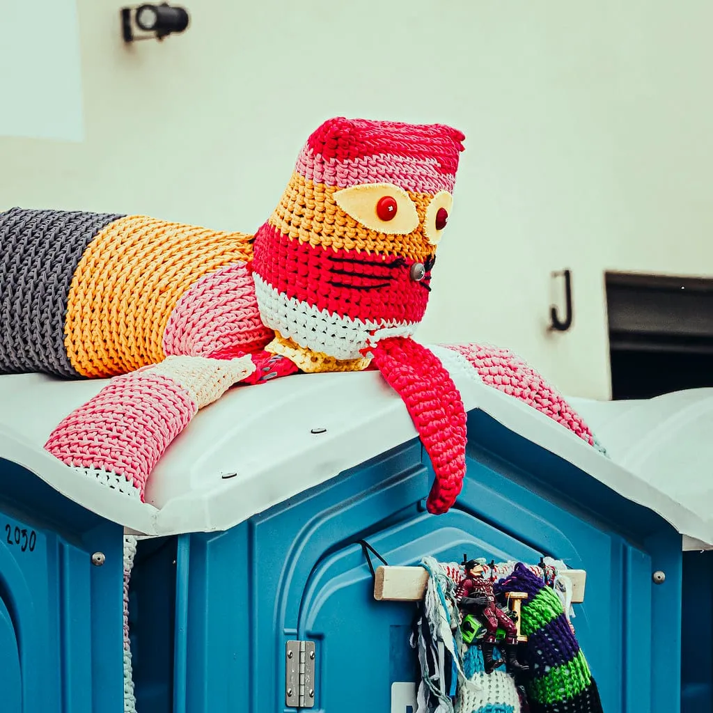 A knitted octopus draped over a portable toilet, one of the BajaMyArt artworks at ODDfest 2025