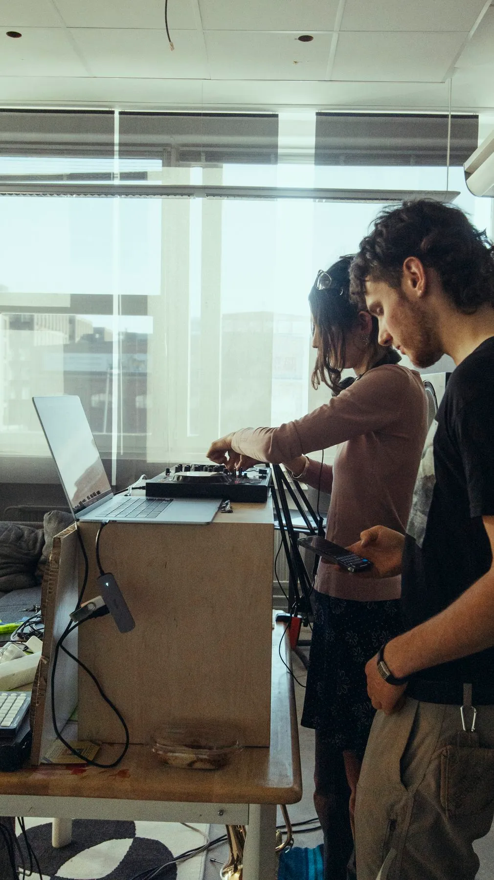 Two DJs playing at a wooden booth by the windows