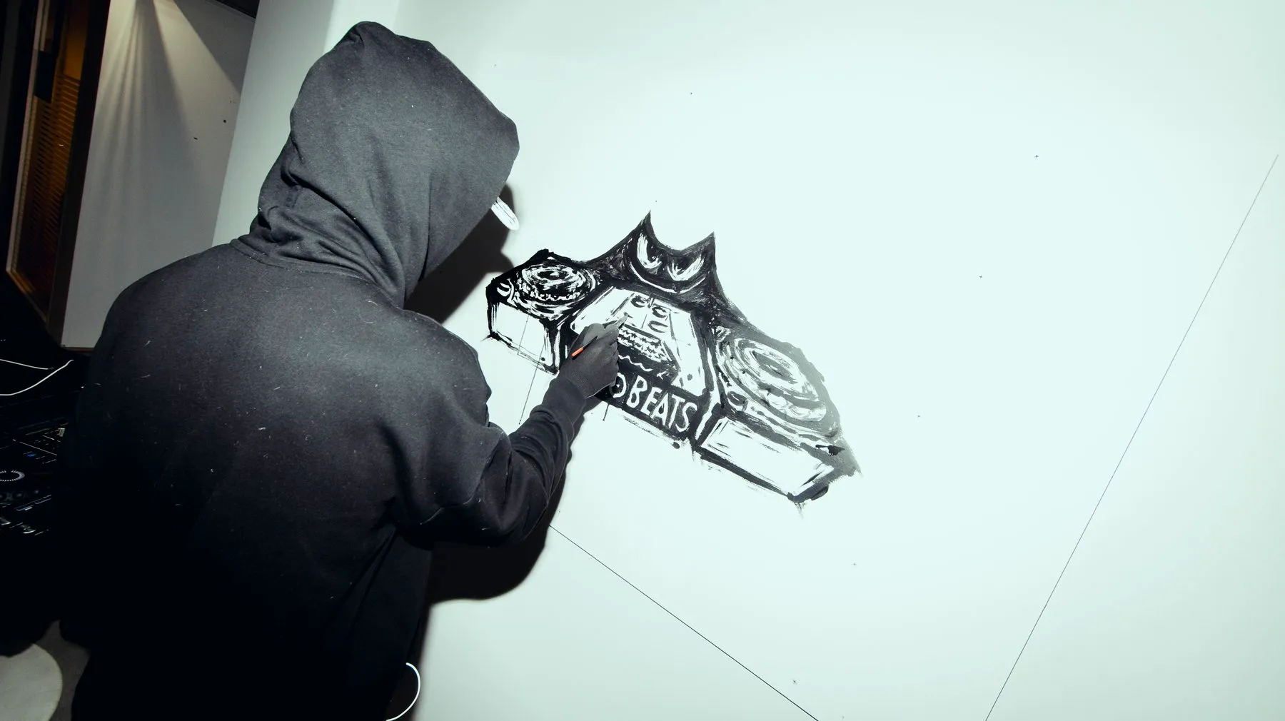 An artist in a hooded top painting a black-ink mural on a white wall at ODDspace