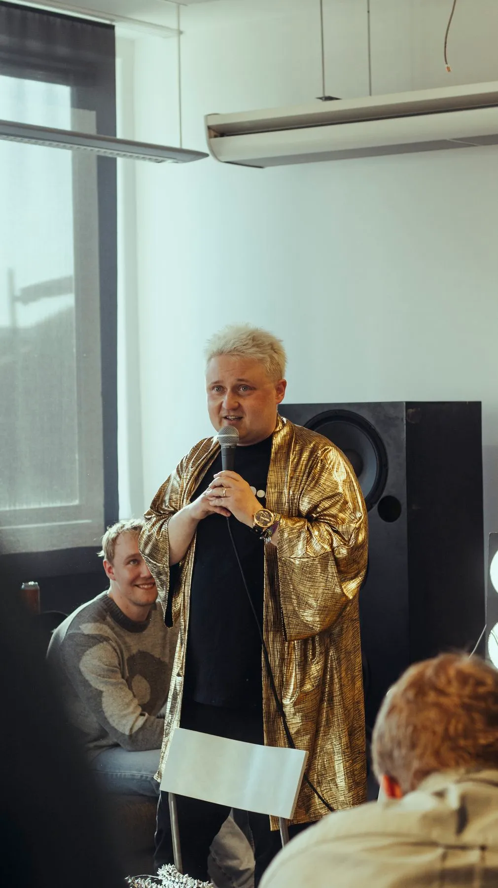 A performer in a gold jacket speaking into a microphone