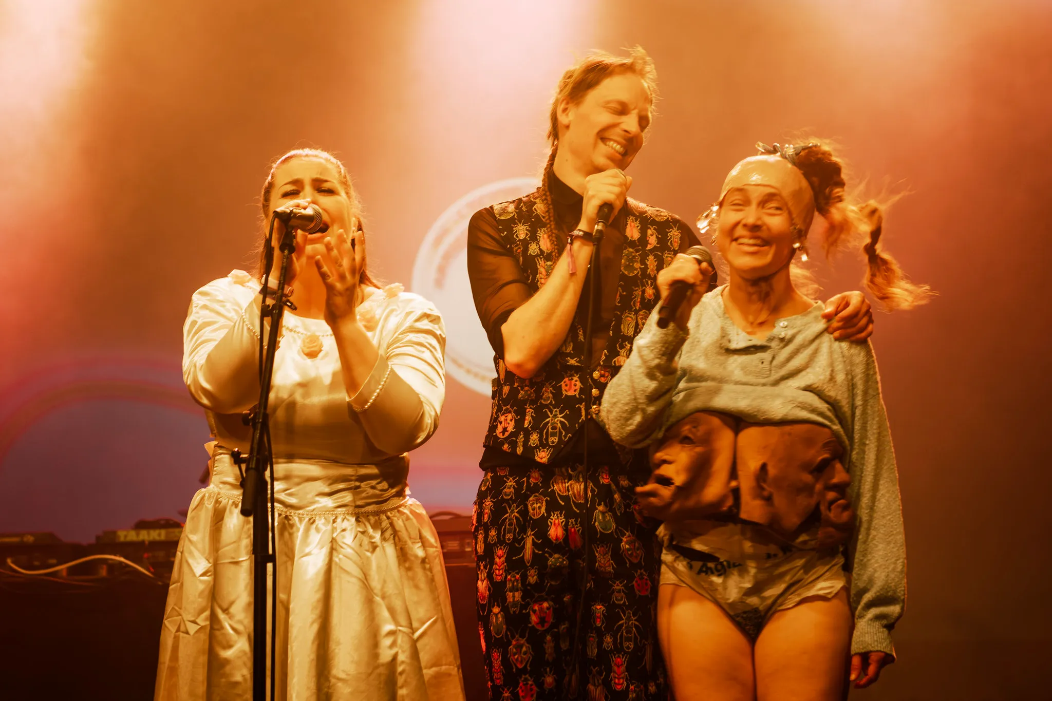 Three performers in gold and cream costume at the microphone