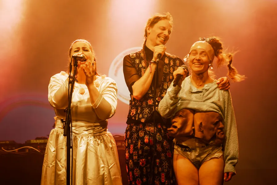 Three performers in gold and cream costume at the microphone